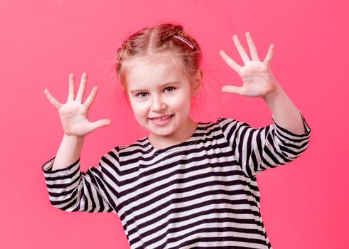 Amusing blonde little girl showing her palms and loooking at camera, pink background