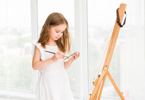 Portrait of surprised little girl painting a picture on canvas. Little child girl draws with watercolor on easel