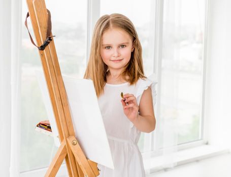 Portrait of a beautiful little girl drawing on easel. Creative child girl making a picture
