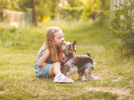 Cute little child girl sitting on the grass with her little Yorkshire terrier dog in the park