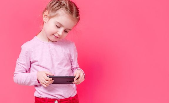 Adorable stylish small girl using smartphone over pink background