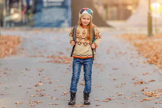 Cute school girl with leaves and backpack on park road