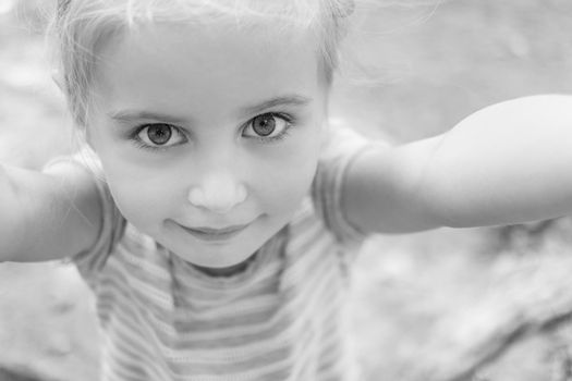 Cute little girl with big eyes smiles making selfie, black and white photo.