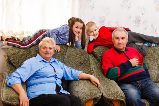 Happy young boy and girl with their laughing grandparents smiling at the camera as they pose together indoors