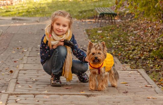 Happy girl next to yorkshire terrier in autumn park