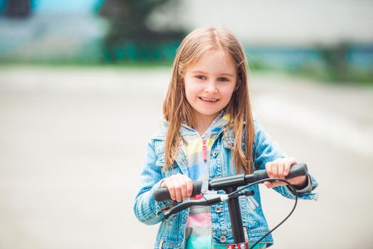 Small happy toddler girl with cool modern scooter on blurry background