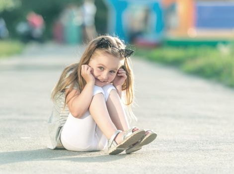 Little happy girl is sitting on the street