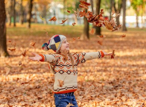 Cute little girl throwing up autumn leaves in park