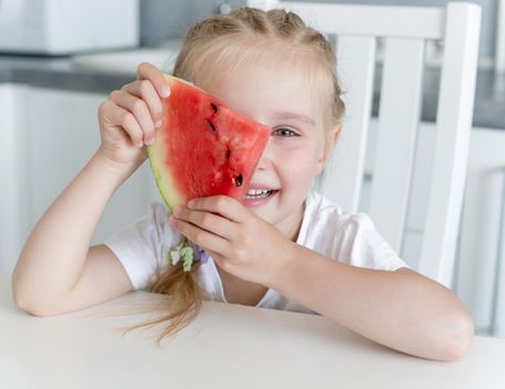 cute little girl eats a watermelon at home in the kitchen