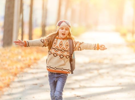 Happy schoolgirl with backpack going home across sunny park