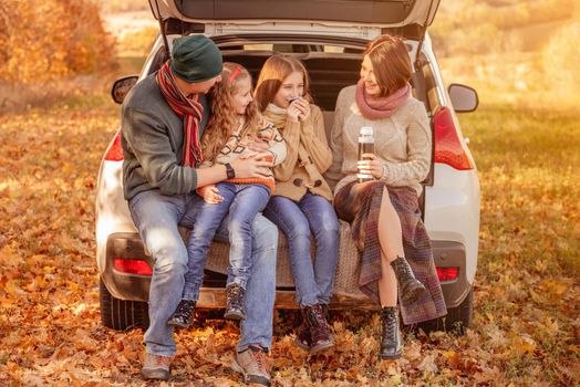 Happy family sitting in car trunk on autumn background