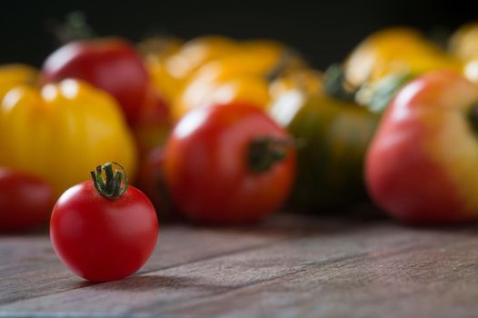 Cherry tomato on rustic wooden background with colorful tomatoes in backround. Shallow depth of field.