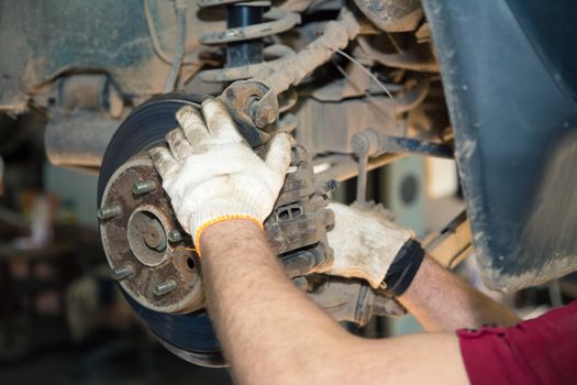 The gloved hands of a man unscrew the caliper on the hub. In the garage, a man changes parts on a vehicle. Small business concept, car repair and maintenance service. UHD 4K.