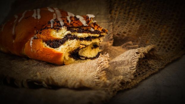 Fresh poppy seed roll on natural linen napkin on rustic wooden background