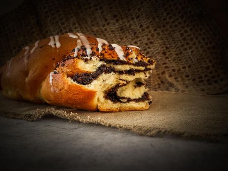 Fresh poppy seed roll on natural linen napkin on rustic wooden background