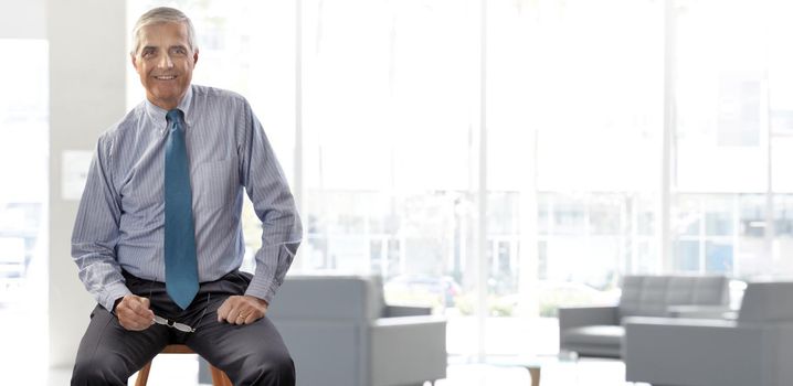 Senior businessman sitting on a stool in a modern high key office setting.