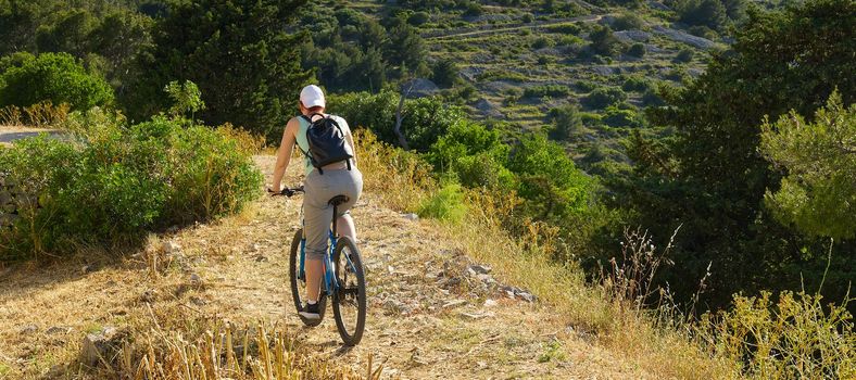 A woman cyclist rides along a mountain path on her mountain bike on a summer sunny day. activity. extreme sport