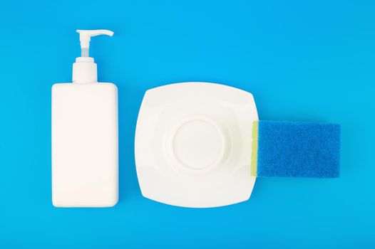 Creative dishwashing concept, top view of detergent, cleaning sponge and clean plate on blue background