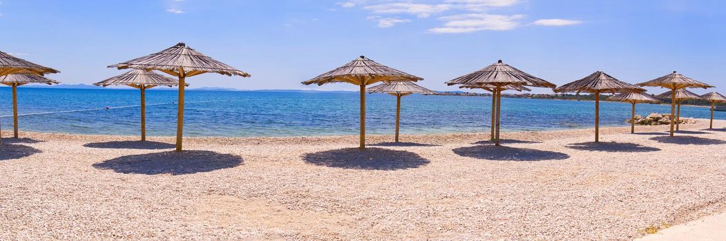 Empty Beach in Croatia. Sunshades on blue sky background on Adriatic seashore . Summer background wide banner.