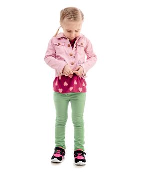 Adorable child trying to zip her pink coat, wearing green pants, isolated on white background