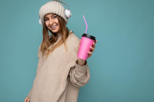 Photo of sexy attractive young happy smiling blonde woman wearing everyday stylish clothes isolated over colourful background wall holding paper cup for cutout drinking tea looking at camera. empty space