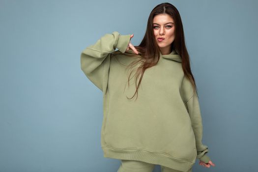 Photo of beautiful young brunette cool woman in a stylish khaki hoodie isolated on blue background. Mockup. Empty space.