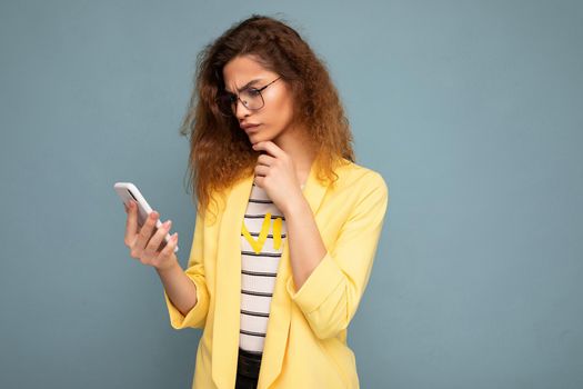 Beautiful young woman wearing casual clothes standing isolated over background surfing on the internet via phone looking at mobile screen.