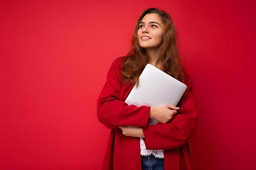 Photo of mysterious pretty young dark hair curly female student holding close netbook wearing red cardigan and white blouse looking to the side isolated over red background.