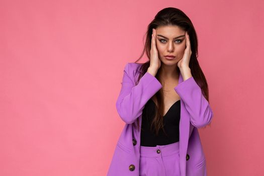 Portrait of young self-confident serious concentrated attractive fashionable brunette woman wearing stylish violet suit isolated on pink background with empty space. Business concept.