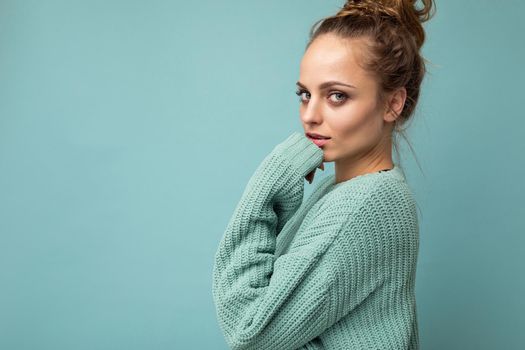 Young beautiful cute curly blonde woman with sexy expression, cheerful and happy face wearing trendy blue sweater isolated over blue background with copy space.