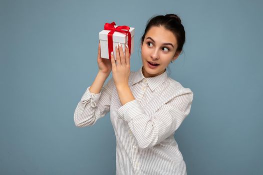 Shot of attractive positive smiling young brunette woman isolated over colourful background wall wearing everyday trendy outfit holding gift box and looking to the side.