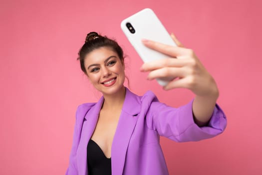 Attractive charming young smiling happy woman holding and using mobile phone taking selfie wearing stylish clothes isolated over wall background.