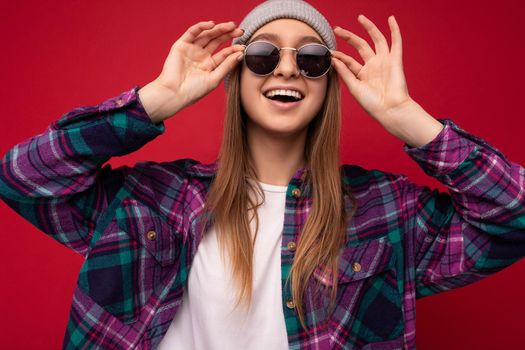 Photo shot of beautiful positive young brunette woman wearing summer casual clothes and stylish sunglasses isolated over colorful background wall looking at camera.