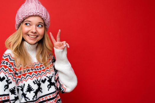 Photo of young positive happy smiling beautiful woman with sincere emotions wearing stylish clothes isolated over background with copy space and showing peace gesture.