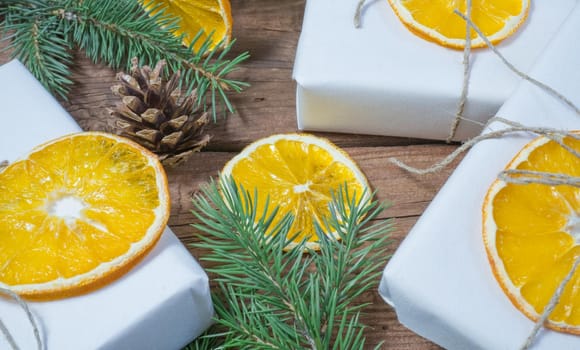 Christmas presents or gift box wrapped in kraft paper with decorations, pine cones, dried orange orange slices and fir branches on a rustic wooden background. Holiday concept