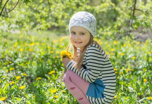 Pretty little kid in white cute hat sitting in the garden with yellow bright flowers