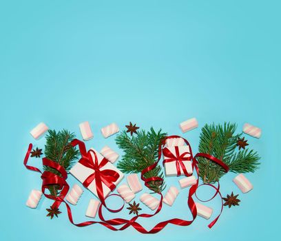 Christmas Holiday Composition. New Year Gift in White Box with Red Ribbon Fir Tree Branches Star Anise Marshmallows on Blue Background Flat Lay Top View with Copy Space For Your Text