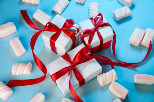 Christmas Holiday Composition. New Year Gift White Boxes Red Ribbon with Marshmallows on Blue Background. Flat Lay.