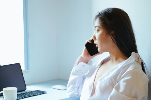 The new normal. A businesswoman is using her phone and computer to work for a company. over the Internet on your desk at home