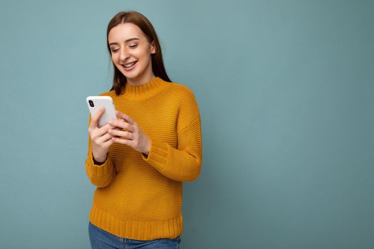 Beautiful young woman wearing casual clothes standing isolated over background surfing on the internet via phone looking at mobile screen.