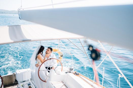 The bride and groom stand at the helm of the yacht sailing in the sea and embrace . High quality photo