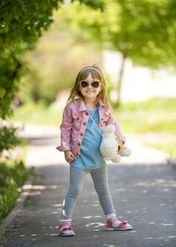 trendy little girl in park with teddybear in hand with sunglasses
