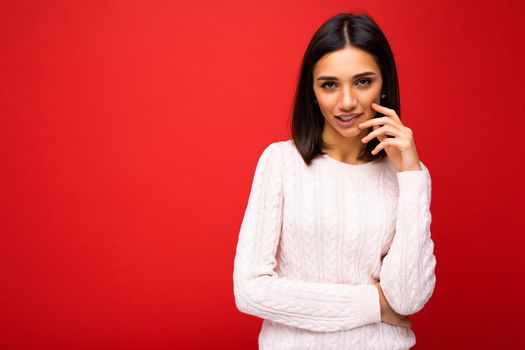 Portrait of young thoughtful sexy beautiful brunette woman with sincere emotions wearing casual sweater isolated over red background with copy space.