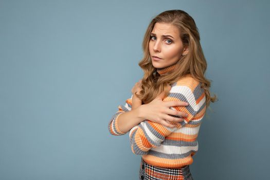 Photo shot portrait of young nice winsome beautiful sad upset sorrowful deplorable blond woman with sincere emotions wearing striped sweater isolated over blue background with free space.