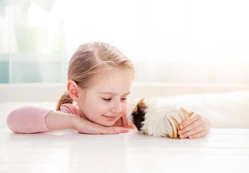 Portrait of happy smiling little girl hugging fluffy tricolor guinea pig. Adorable little child with pet