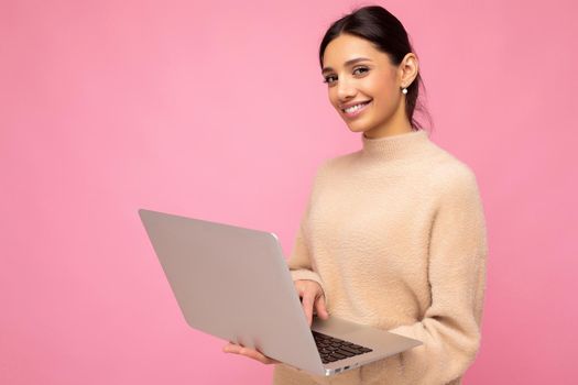 Close-up portrait of Beautiful smiling young brunette woman holding netbook computer looking at camera isolated over pink wall background. copy space