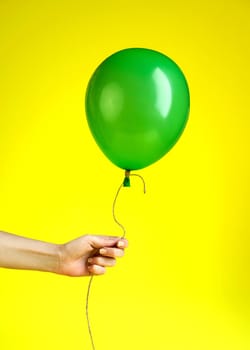 Woman Holding in Hand a Green Balloon on Yellow Background.