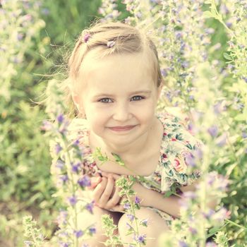 Sweet little girl sitting in field full of herbs and small flowers, summer, smiling, closeup