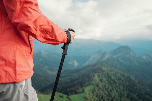 Unrecognizable hiker young woman with trekking poles walking in summer mountains.