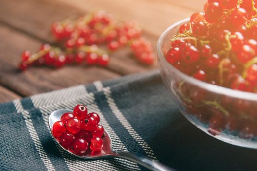 Summer fresh ripe red currant in a glass bowl and on spoon on tablecloth. Berry background.